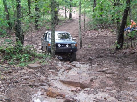 1989 Ford Bronco - A Ford truck navigates a challenging, rocky path through a wooded area.