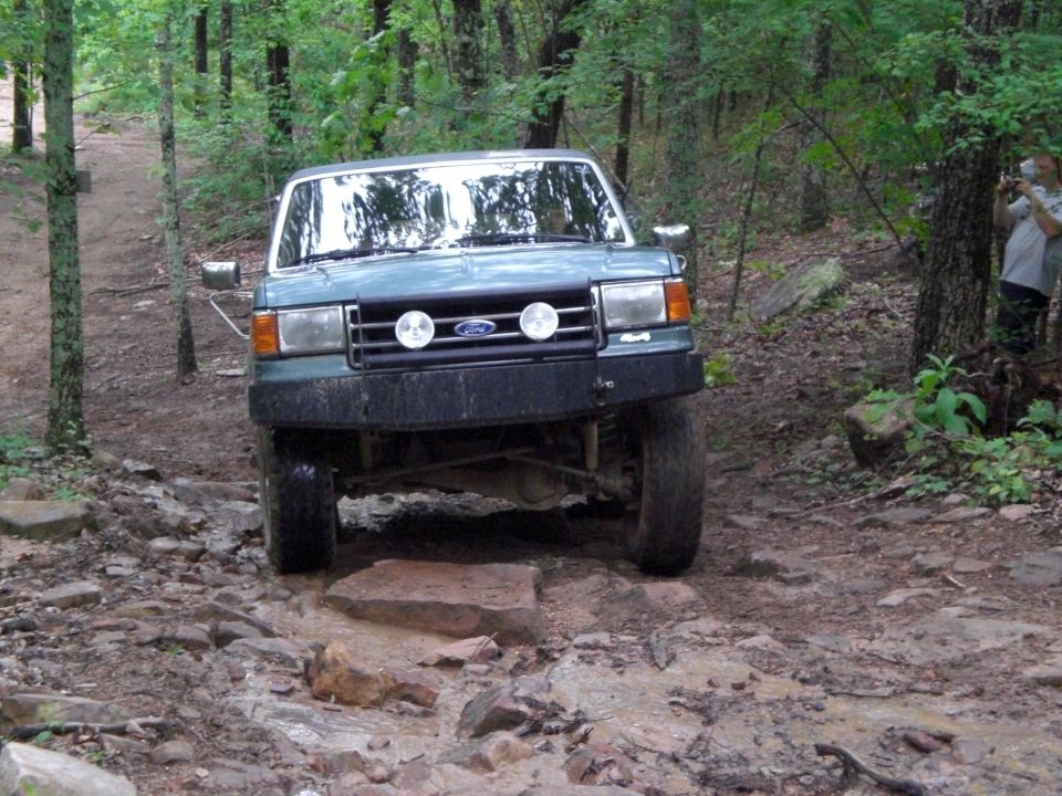 Green Ford Bronco on rocky trail, front view. Modified bumper and off-road tires