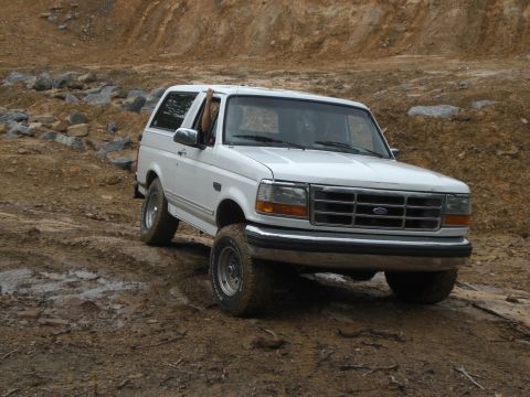 1989 Ford Bronco - A white Ford Bronco navigates a challenging off-road course with a driver's arm visible outside the window.