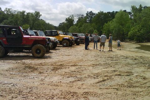 2008 Jeep Wrangler - A group of Jeep Wranglers are parked in a dirt lot with people gathered nearby.