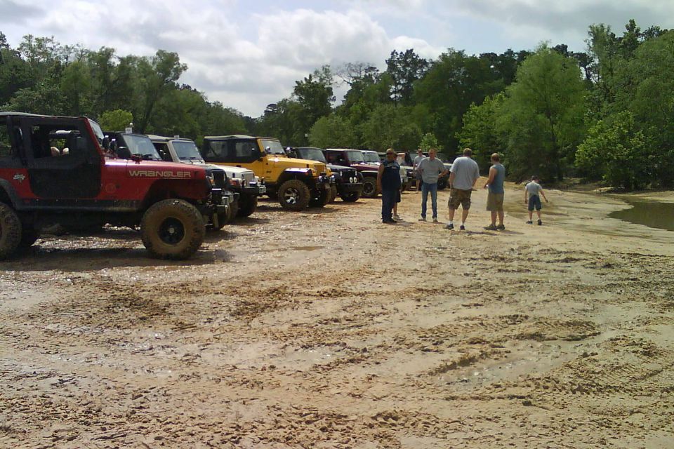 Several Jeep Wranglers parked in a line on a muddy, outdoor area. People are standing around them