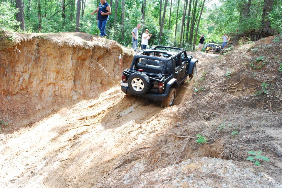 Black 2007 Jeep Wrangler driving on a muddy, rutted trail with people watching