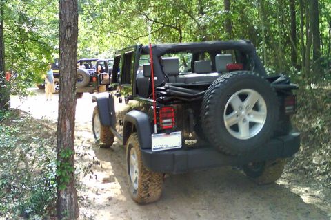 2008 Jeep Wrangler - Multiple black Jeep Wranglers drive on a dirt path through a wooded area.