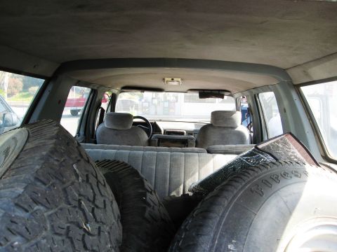 1986 Ford Bronco - Spare tires are loaded into the rear cargo area of an older SUV, obscuring the view of the back seats.