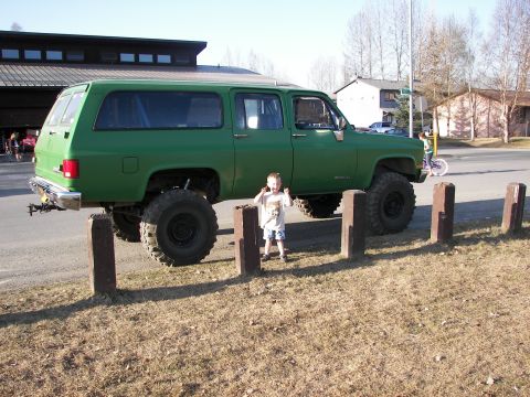 1990 Chevrolet Suburban - A green SUV with oversized tires is parked on the side of the road.