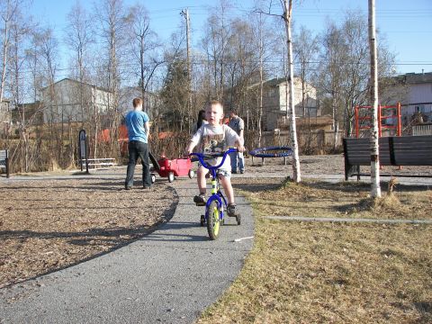 1990 Chevrolet Suburban - A child enjoys a ride on a tricycle in a park setting on a sunny day.