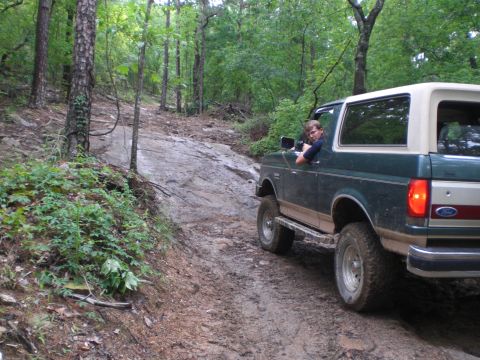 1989 Ford Bronco - A green 1989 Ford Bronco navigates a rocky, wooded trail with a driver behind the wheel.
