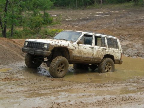 1989 Ford Bronco - Muddy white Jeep Cherokee XJ navigates a challenging off-road course.