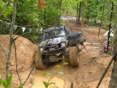 1989 Ford Bronco - Off-road vehicle navigates a muddy trail with a roll cage and winch.