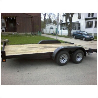 2005 Ford F-250 - A flatbed trailer with a wooden deck and dual axles is parked on a street in front of a house.