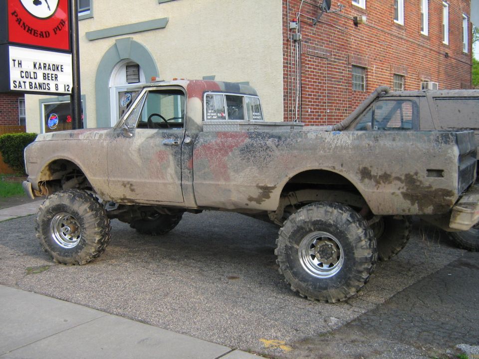 Mud-covered lifted pickup truck with large tires, parked next to another vehicle
