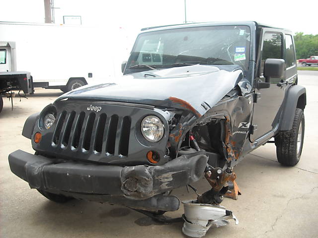 Wrecked dark gray Jeep Wrangler front view with extensive damage to the front passenger side