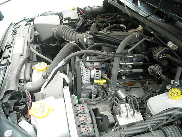 Engine bay of a modern vehicle, showing hoses, wires, alternator, and fuse box