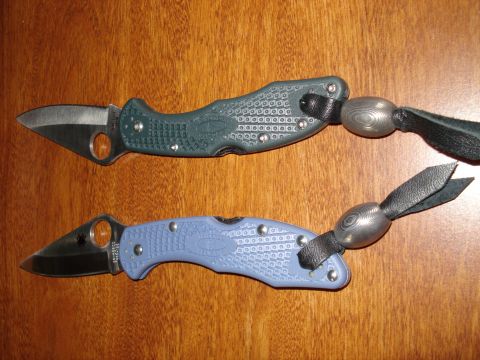 2000 Ford Crown Victoria - Two folding knives are displayed on a wooden surface, each with a lanyard and decorative bead.