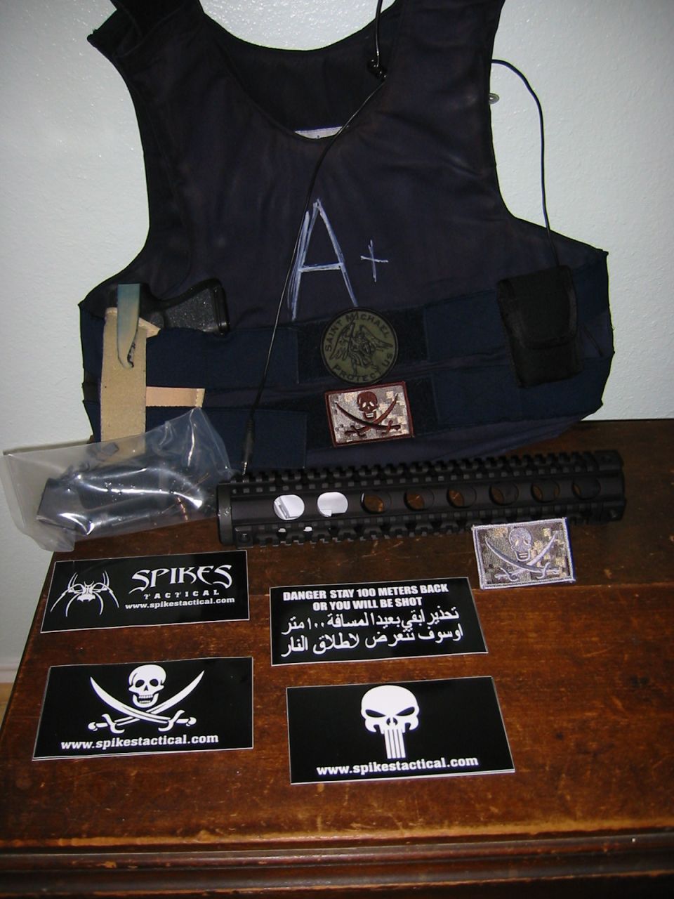 Tactical vest with patches and a rifle handguard on a wooden table