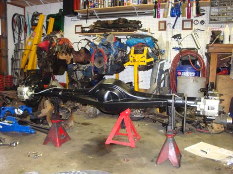 1989 Ford Bronco - A black rear axle assembly is supported by red jack stands in a cluttered garage environment.