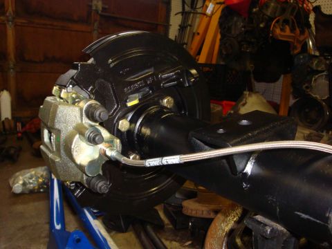 1989 Ford Bronco - Close-up of a rear axle assembly a disc brake caliper and a braided stainless steel brake line.