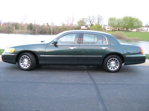1988 Mercury Grand Marquis - This green sedan, likely a 2001 Lincoln Town Car, is viewed from its side against a backdrop of water and trees.