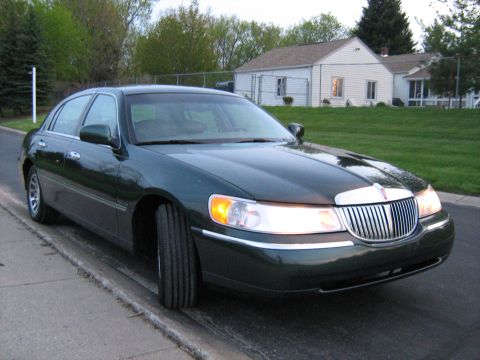 1988 Mercury Grand Marquis - A dark green Lincoln Town Car is parked on the side of the road in front of a house.