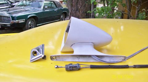 1972 Ford Ranchero - A white side mirror assembly and chrome trim piece are displayed on a yellow surface, with a green car visible in the background.
