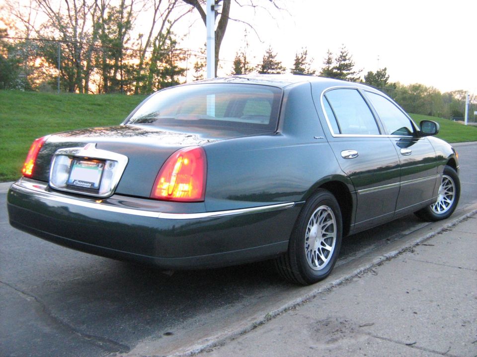Dark green Lincoln Town Car parked on a curb, rear quarter view