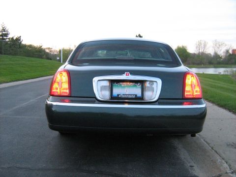 1988 Mercury Grand Marquis - Rear view of a dark green sedan parked on a roadside, chrome accents and distinctive vertical taillights.