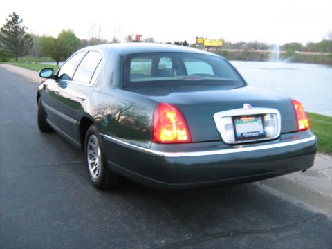1988 Mercury Grand Marquis - A dark green sedan is parked on the side of a road with a lake in the background.