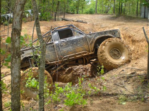 1989 Ford Bronco - This heavily modified pickup truck is navigating a challenging muddy terrain with extreme articulation.