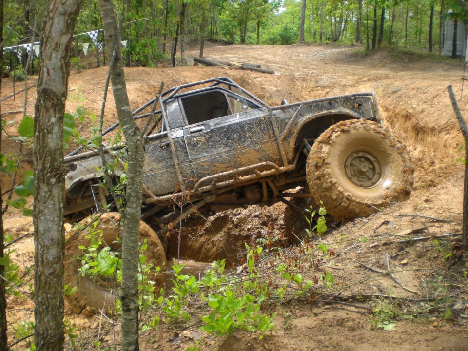 Muddy off-road pickup truck with large tires climbing a dirt hill, roll cage visible