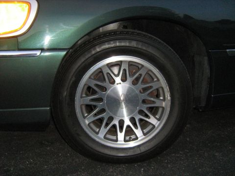 1988 Mercury Grand Marquis - Close-up of a green car's front wheel, a distinctive alloy rim with a Lincoln emblem on the center cap.
