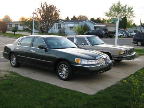 1988 Mercury Grand Marquis - Two sedans are parked on a concrete driveway in front of houses.