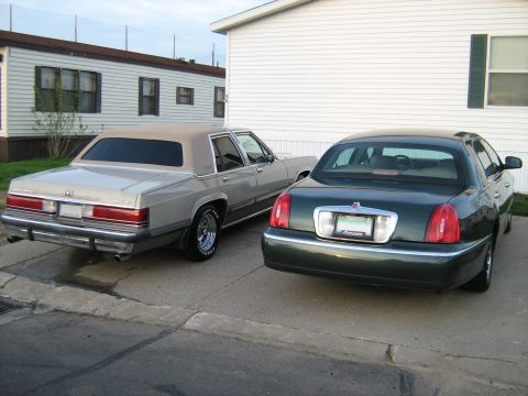 1988 Mercury Grand Marquis - Two sedans, a Lincoln Town Car and a Mercury Grand Marquis, are parked side-by-side in front of a building.