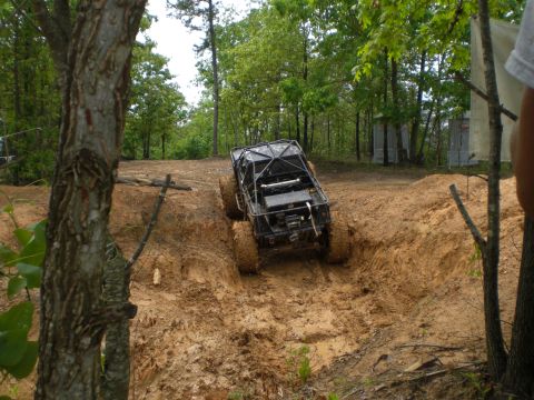 1989 Ford Bronco - A heavily modified off-road vehicle navigates a muddy track in a wooded area.