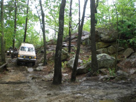 1989 Ford Bronco - A tan van and an ATV navigate a challenging rocky path through a wooded area.