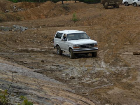 1989 Ford Bronco - A white Ford Bronco navigates a muddy off-road course, with another vehicle in the distance.