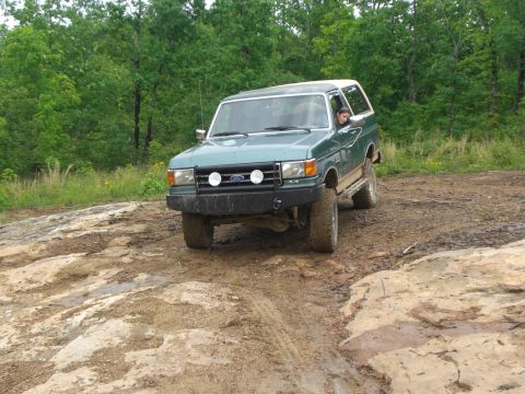 1989 Ford Bronco - This green SUV navigates a challenging muddy and rocky off-road trail, its capabilities.