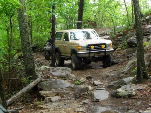 1989 Ford Bronco - A tan 1989 Ford Bronco tackles a challenging rocky trail, with an ATV following closely behind.