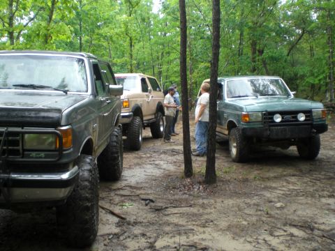 1989 Ford Bronco - Several off-road vehicles are gathered on a wet, wooded path.