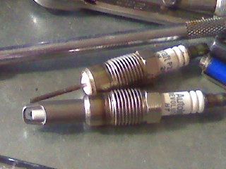 2007 Ford Mustang - Close-up view of two spark plugs, identified as Auto-Lite Platinum, on a workbench.
