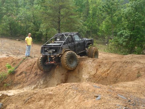 1989 Ford Bronco - Custom off-road truck navigates a steep dirt incline during an outdoor event.