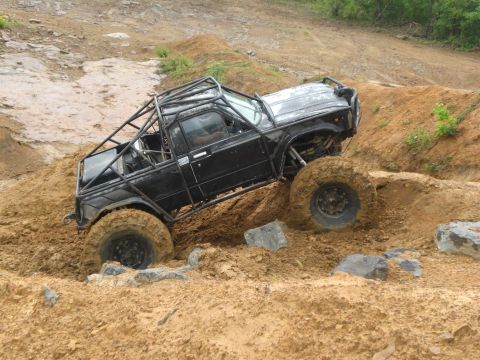1989 Ford Bronco - This heavily modified pickup truck navigates a challenging muddy terrain with large off-road tires.