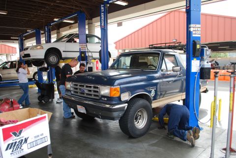 1986 Ford Bronco - Mechanics work on a blue Ford Bronco and a white car in an auto repair shop.