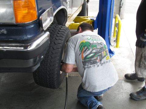1986 Ford Bronco - A person airs up the tire of a blue SUV in a service bay.