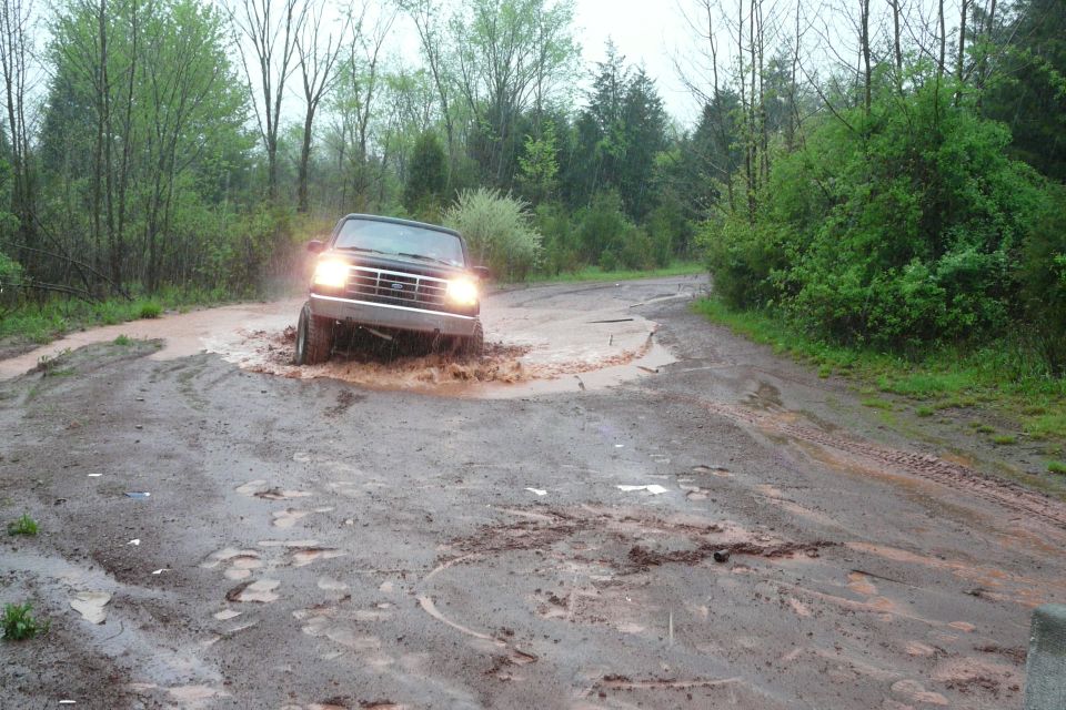 Ford Bronco driving through a muddy puddle on a dirt road