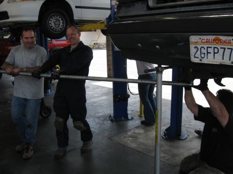 1986 Ford Bronco - Mechanics work on a 1986 Ford Bronco in a garage, with another vehicle lifted above.