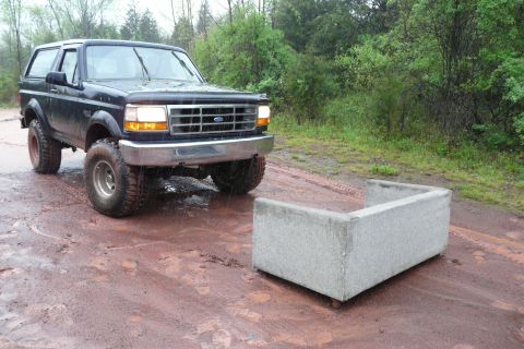 1995 Ford Bronco - A black 1995 Ford Bronco with off-road tires sits on a muddy track next to a concrete structure.