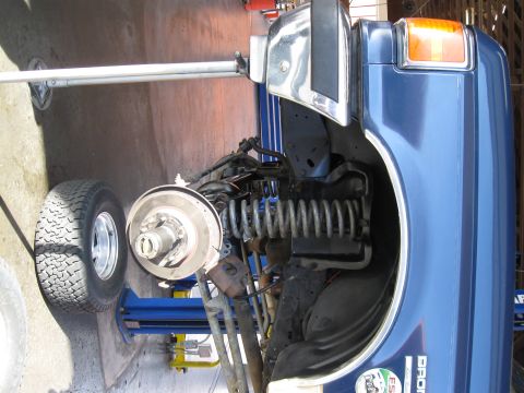1986 Ford Bronco - Front wheel assembly of a blue 1986 Ford Bronco undergoing service on a lift.