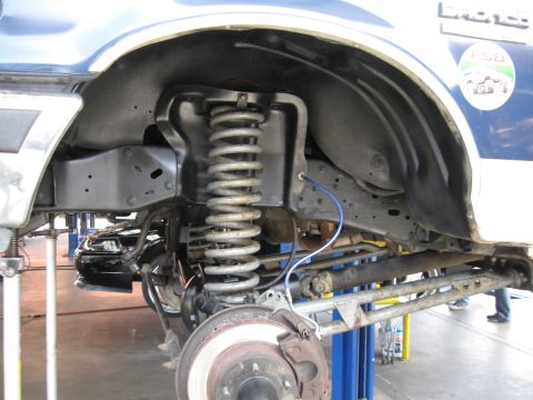 1986 Ford Bronco - Close-up of a lifted vehicle's suspension system, with another car in the background.