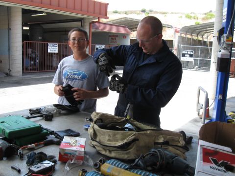 1986 Ford Bronco - Two people are gathered around a table covered in tools and car parts, possibly preparing for a repair.