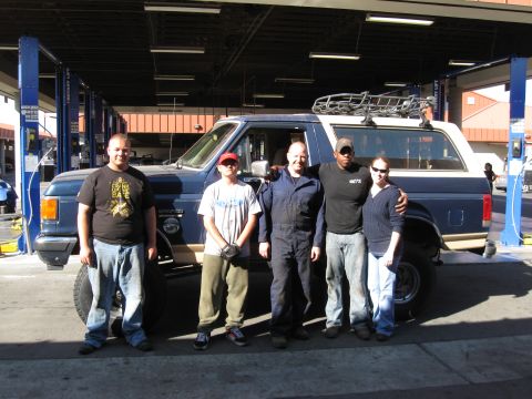 1986 Ford Bronco - A group poses in front of a lifted Ford Bronco in a service bay.